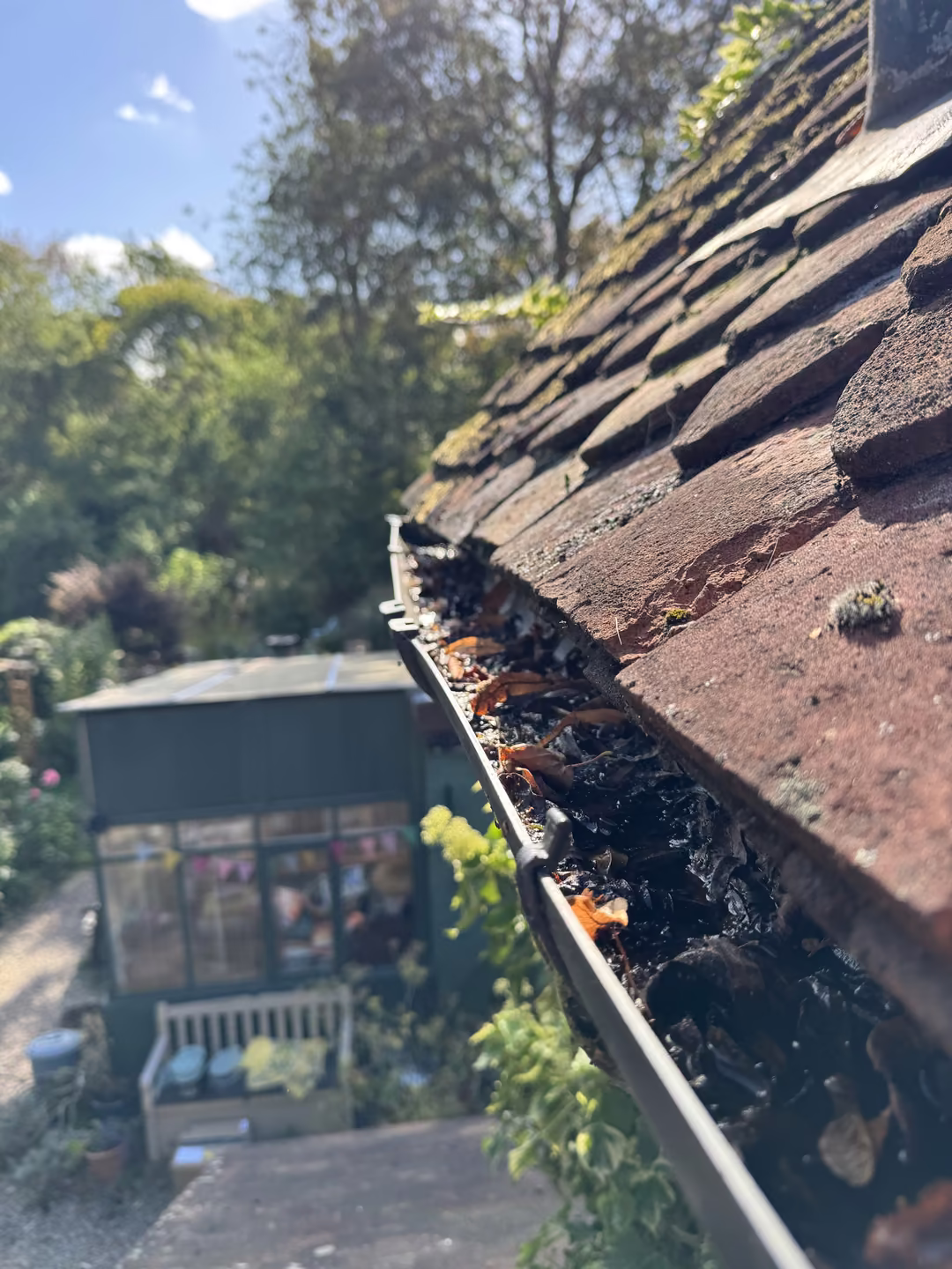 Blocked gutter full of leaves along a clay tile roof before a Just Jets gutter clean