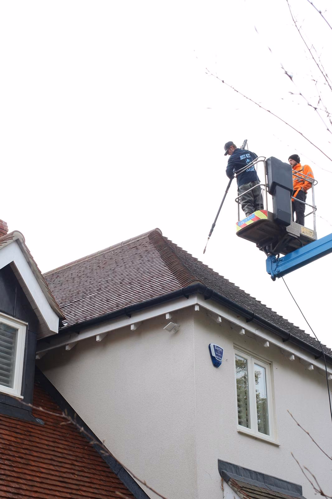 Just Jets team cleaning a tiled roof from a cherry picker above a white-rendered house in Essex